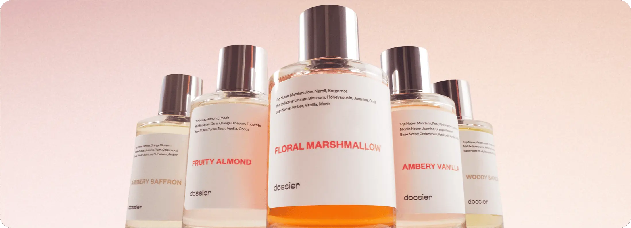 Five Dossier perfume bottles, including Floral Marshmallow, Fruity Almond, Ambery Vanilla, Ambery Saffron, and Woody Sandalwood, arranged against a soft pink background.