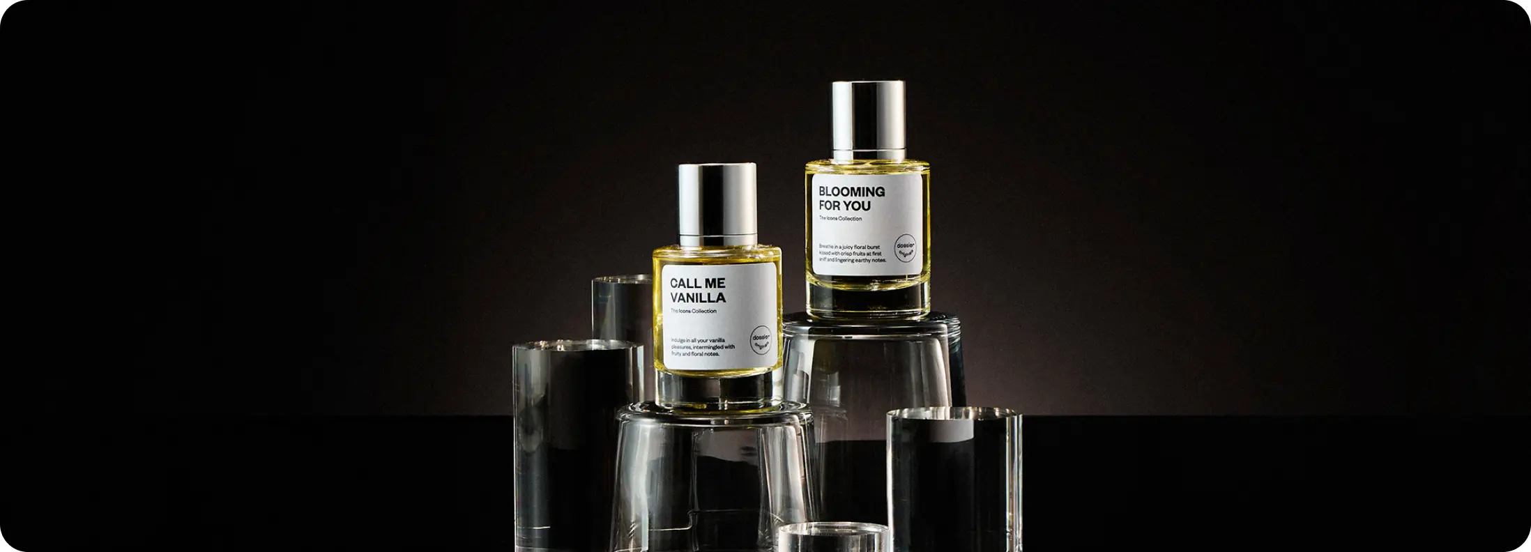 Dossier Call Me Vanilla and Blooming for You perfumes displayed on glass pedestals against a dark background.