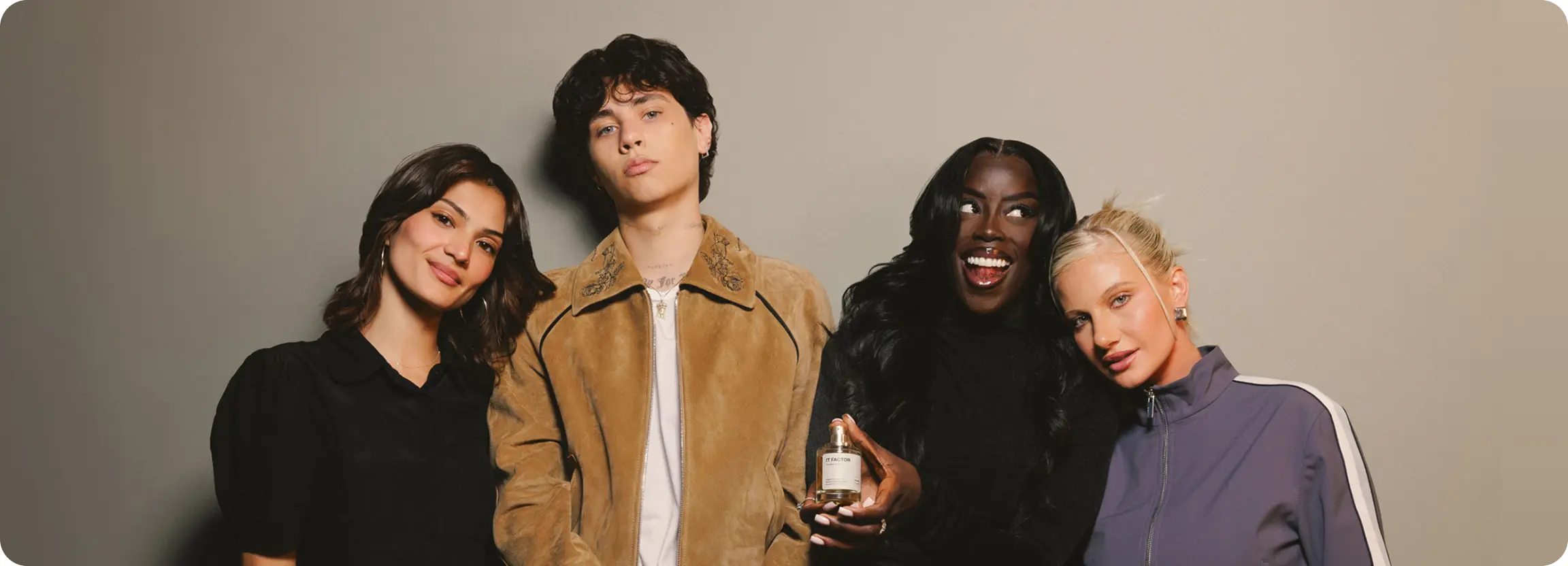 Four models posing together, with one holding a bottle of Dossier It Factor perfume.