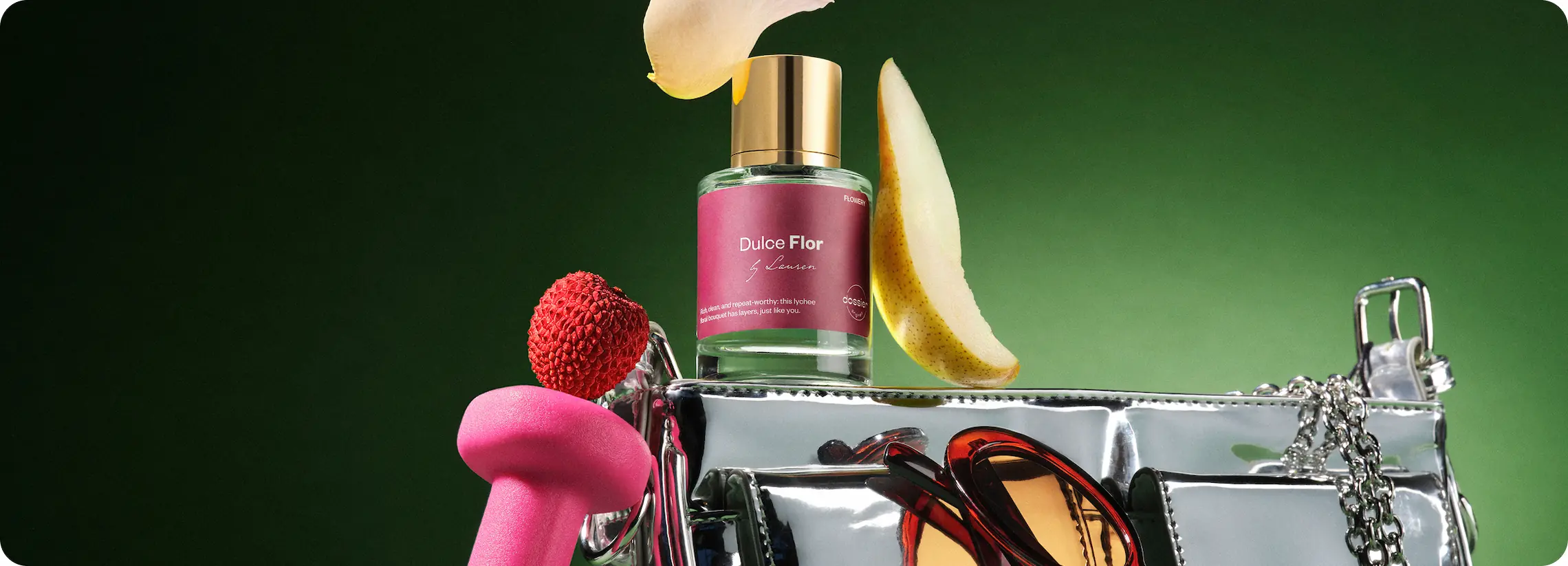Dossier Dulce Flor perfume displayed with lychee, pear slices, sunglasses, and a silver handbag against a green background.