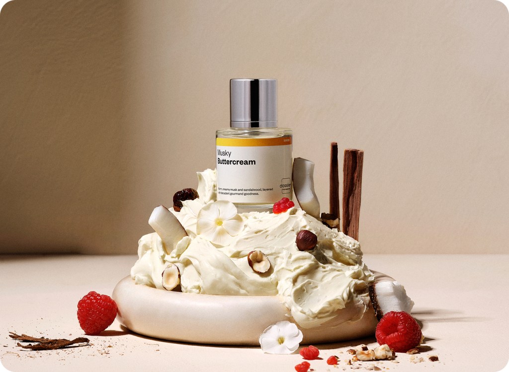 Bottle of 'Musky Buttercream' with a cake and berries on a neutral background