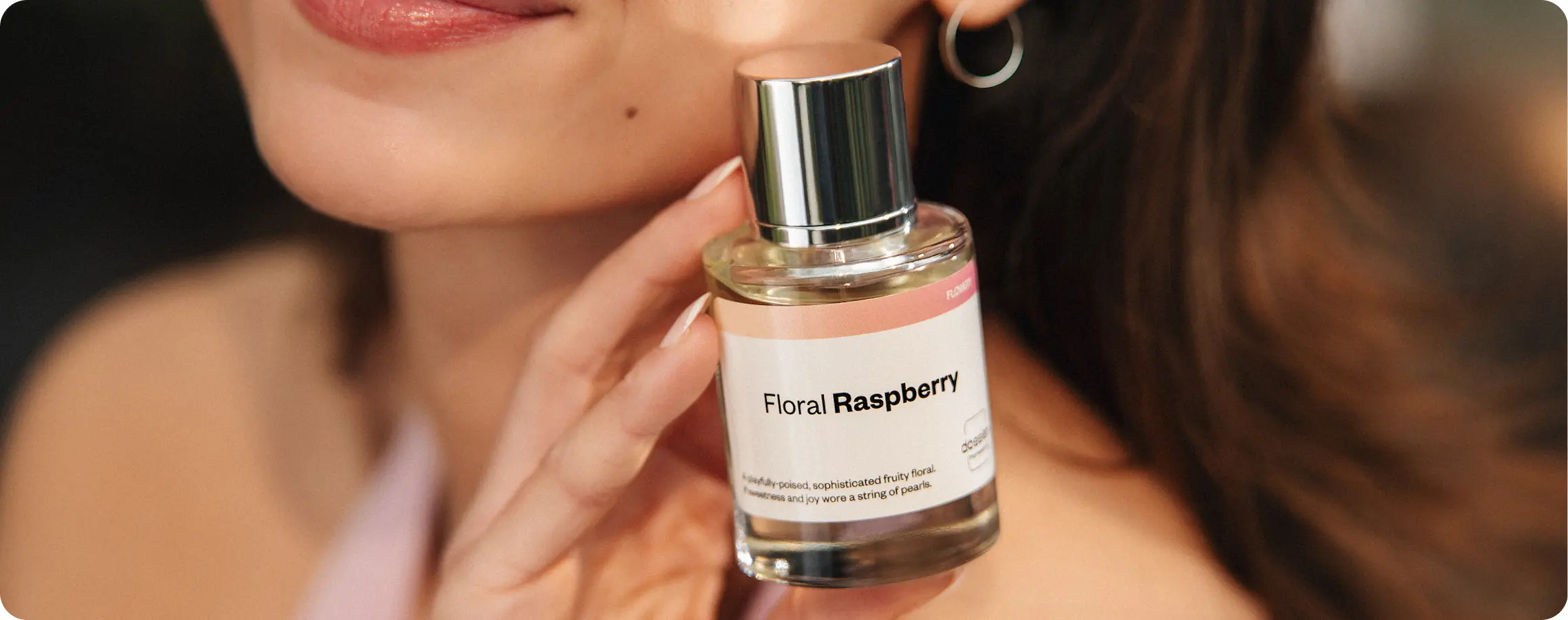 Woman holding a bottle of Dossier Floral Raspberry perfume near her face.
