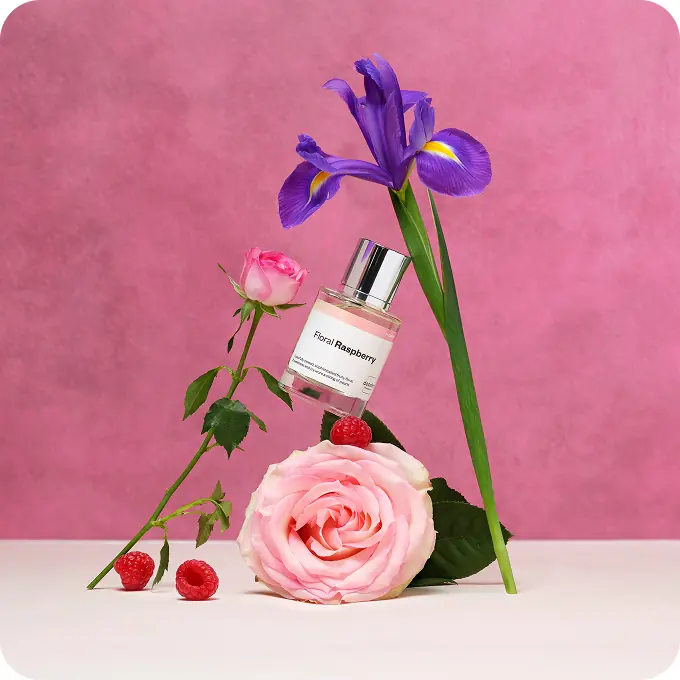 Dossier Floral Raspberry perfume displayed with pink roses, raspberries, and a purple iris against a pink background.