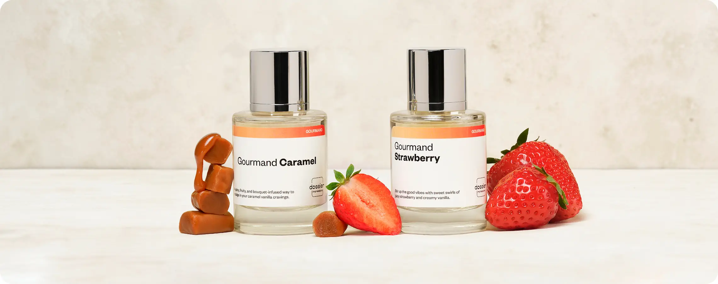 Two Dossier perfumes, Gourmand Caramel and Gourmand Strawberry, displayed with caramel pieces and fresh strawberries
