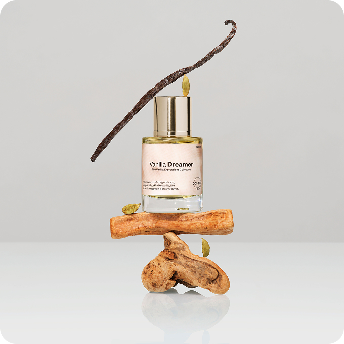 Vanilla Dreamer perfume bottle displayed on sculptural pieces of wood, surrounded by a vanilla pod and cardamom seeds.