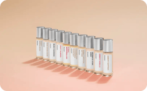 Dossier discovery set featuring assorted perfume travel sprays arranged in a row on a soft peach background.